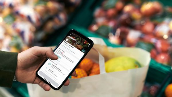 A phone opened on the Too Good to Go app looms over fresh produce in a Morrisons supermarket.