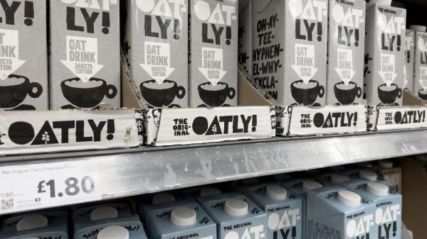 rows of Oatly brand oat milk stacked on a supermarket shelf.