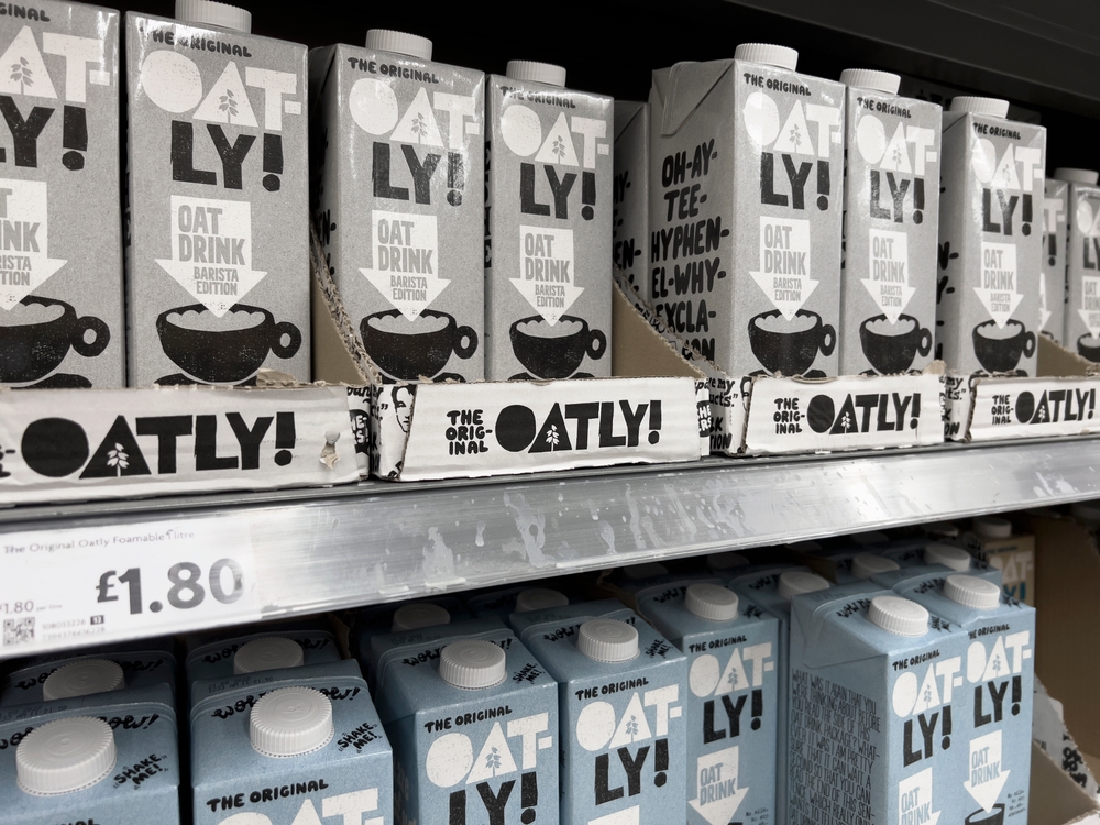 rows of Oatly brand oat milk stacked on a supermarket shelf.
