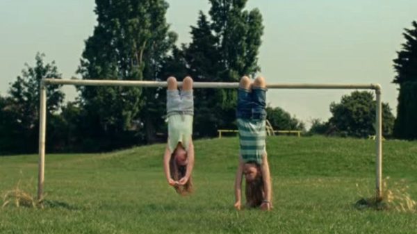 Two girls hanging upside down from a football goal post