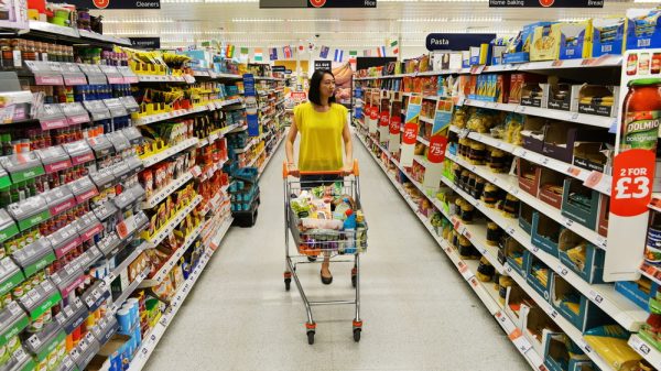 A person walks down a supermarket aisle, browsing shelved items.