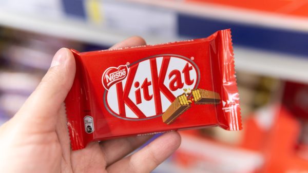 A hand holds up a bar of Nestle's KitKat chocolate.