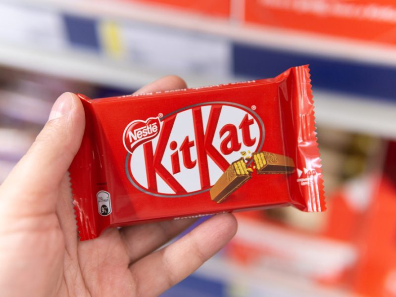 A hand holds up a bar of Nestle's KitKat chocolate.