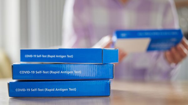 A stack of lateral flow test kits sit before a woman.