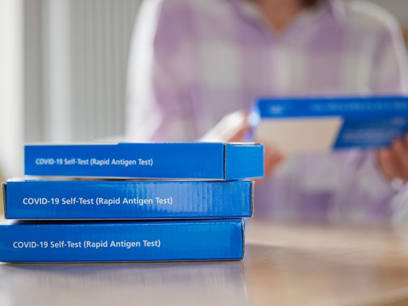 A stack of lateral flow test kits sit before a woman.