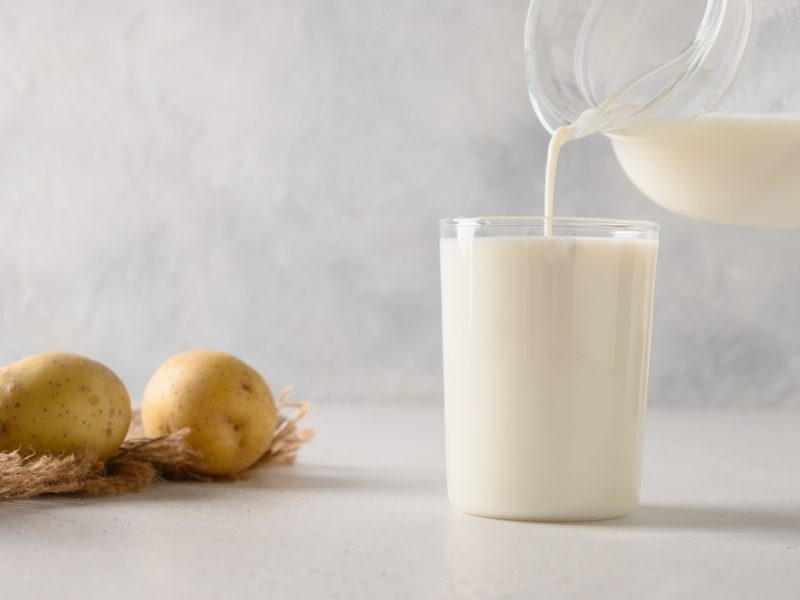 A bag potatoes lie next to a glass of potato milk.