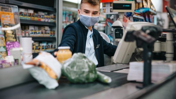 A supermarket worker wears a mask as they work at the tills.