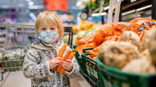 A child holds three carrots in a supermarket.