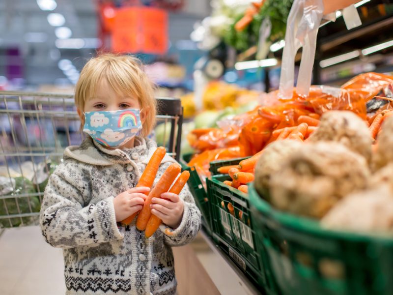 A child holds three carrots in a supermarket.
