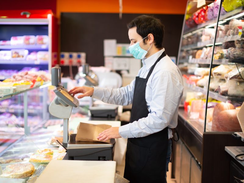 A shop worker wears a mask behind a supermarket counter.