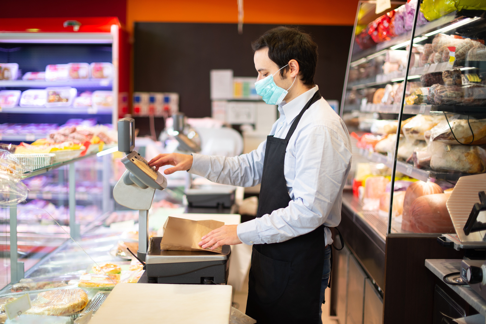 A shop worker wears a mask behind a supermarket counter.