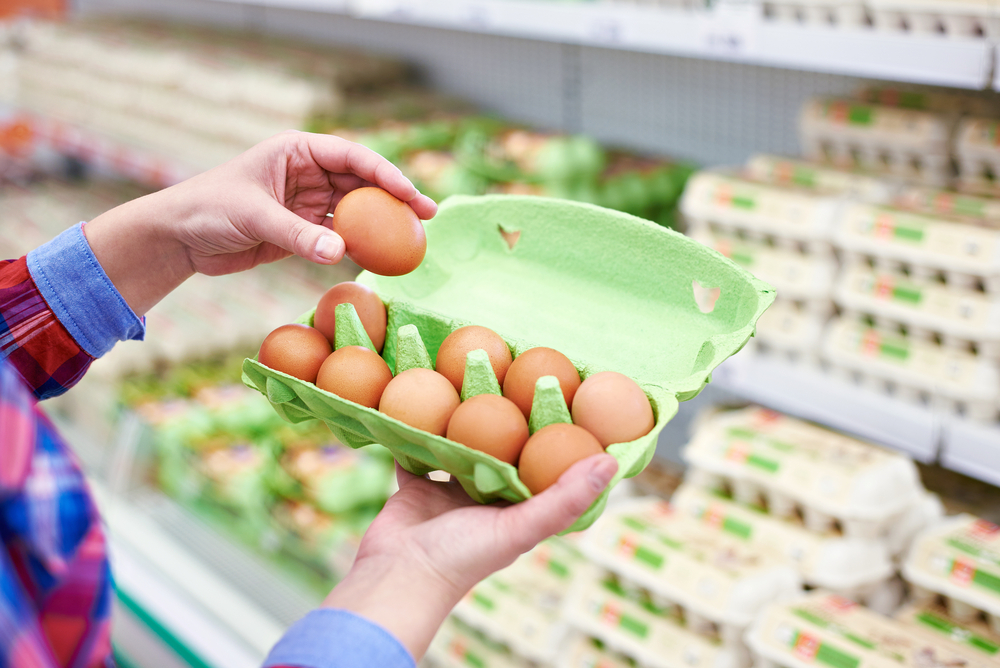 A hand picks out an egg from a carton in a supermarket.
