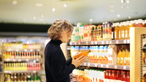 customer looking at a drink in a supermarket, determining whether to add it to shopping basket
