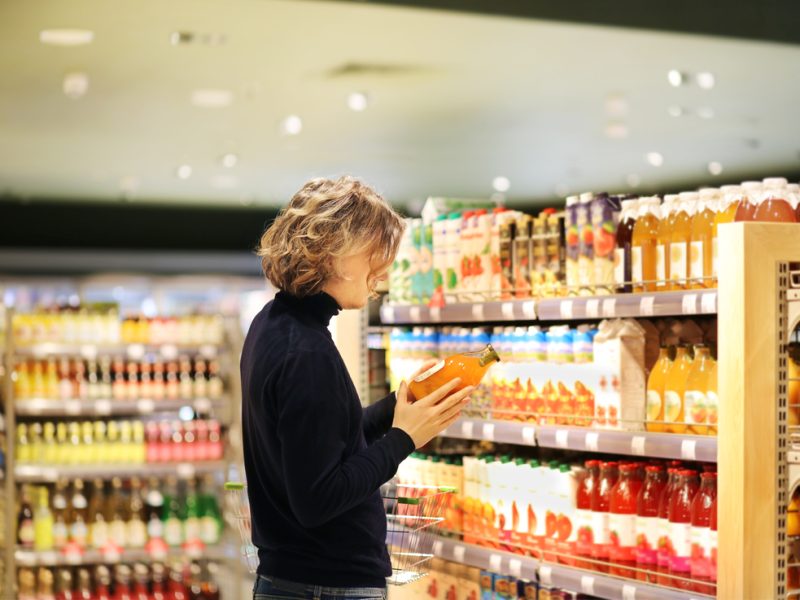 customer looking at a drink in a supermarket, determining whether to add it to shopping basket