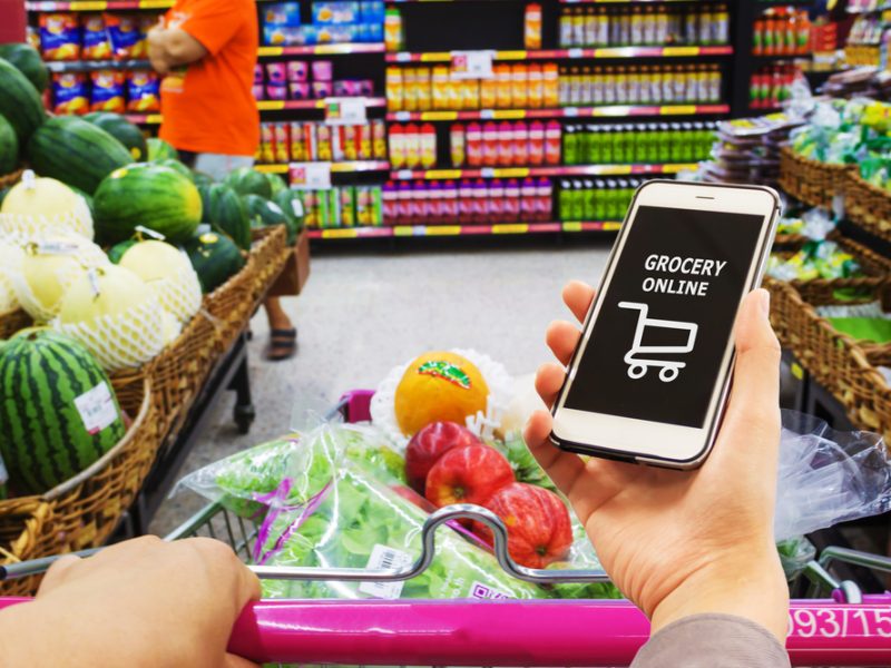 Customer shopping in a supermarket but using online grocery app as well