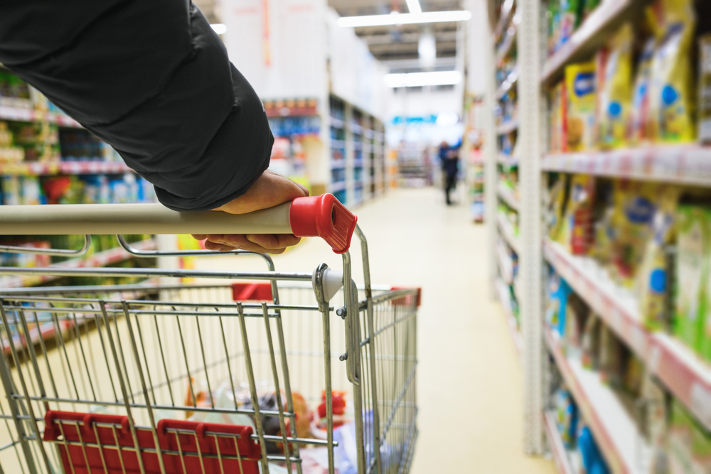 A hand pushes a trolley down a supermarket aisle.