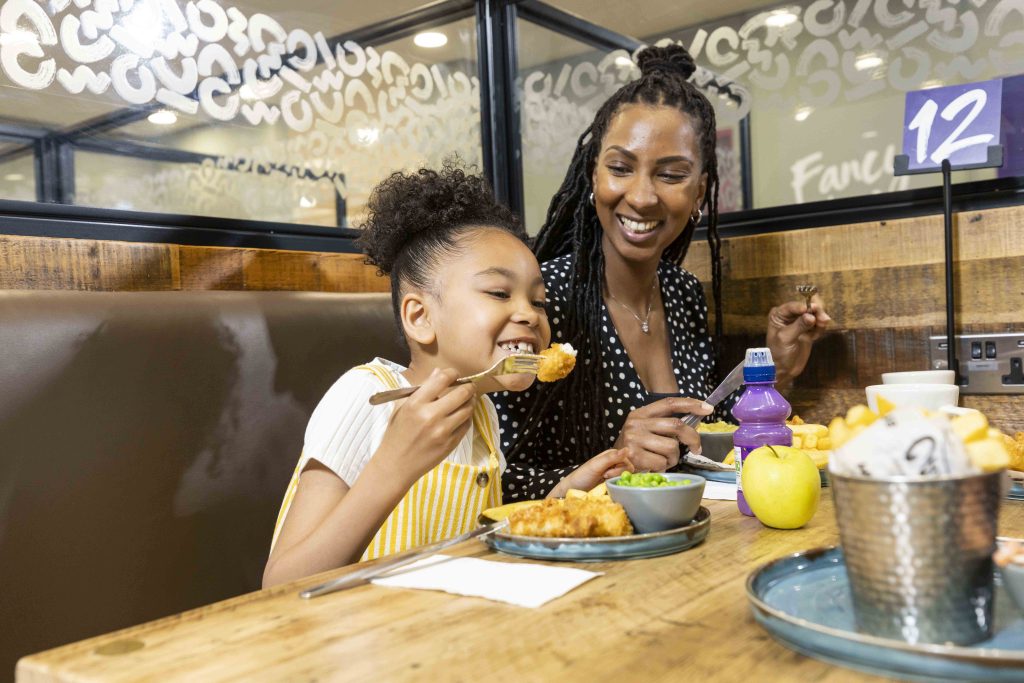 Morrisons is supporting families over the festive period with a new 'Kids Eat Free' initiative available at its cafés nationwide, here depicting a mother and a child eating under the new scheme