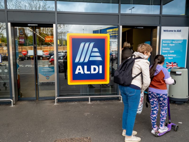 Aldi has revealed another round of price cuts across its range of fresh produce and everyday grocery essentials, here depicting and Aldi store with two customers outside