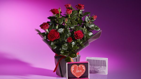 Waitrose has partnered with Biscuiteers for an exclusive biscuit and bouquet Valentine's range, here depicting a Waitrose bunch of red roses with a Biscuiteers luxury gift and card. It is in front of a purple background.